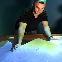 Personne formant des volumes dans le sable pour interagir avec le mapping video